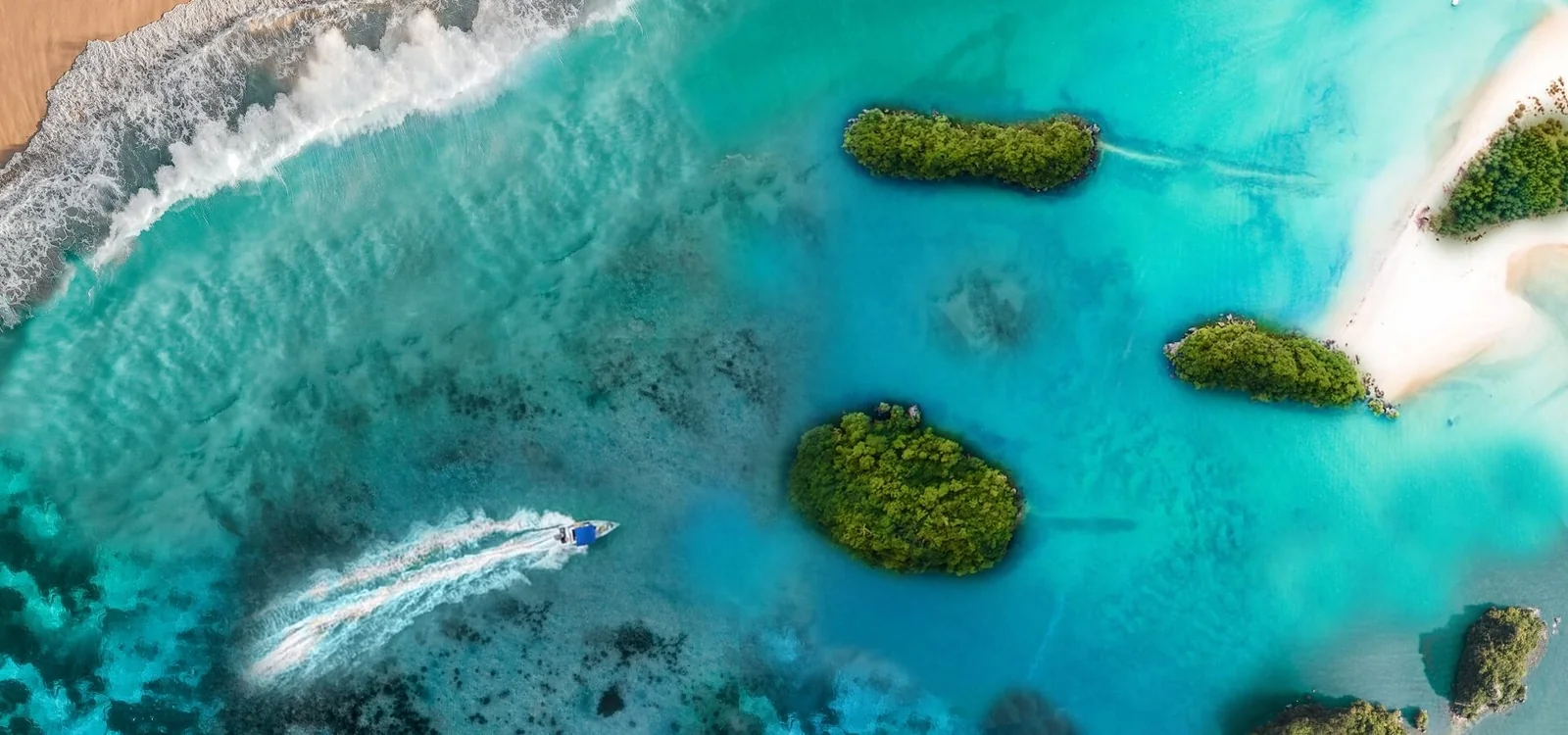 Vue aérienne d’un bateau près d’îlots arborés dans un lagon turquoise